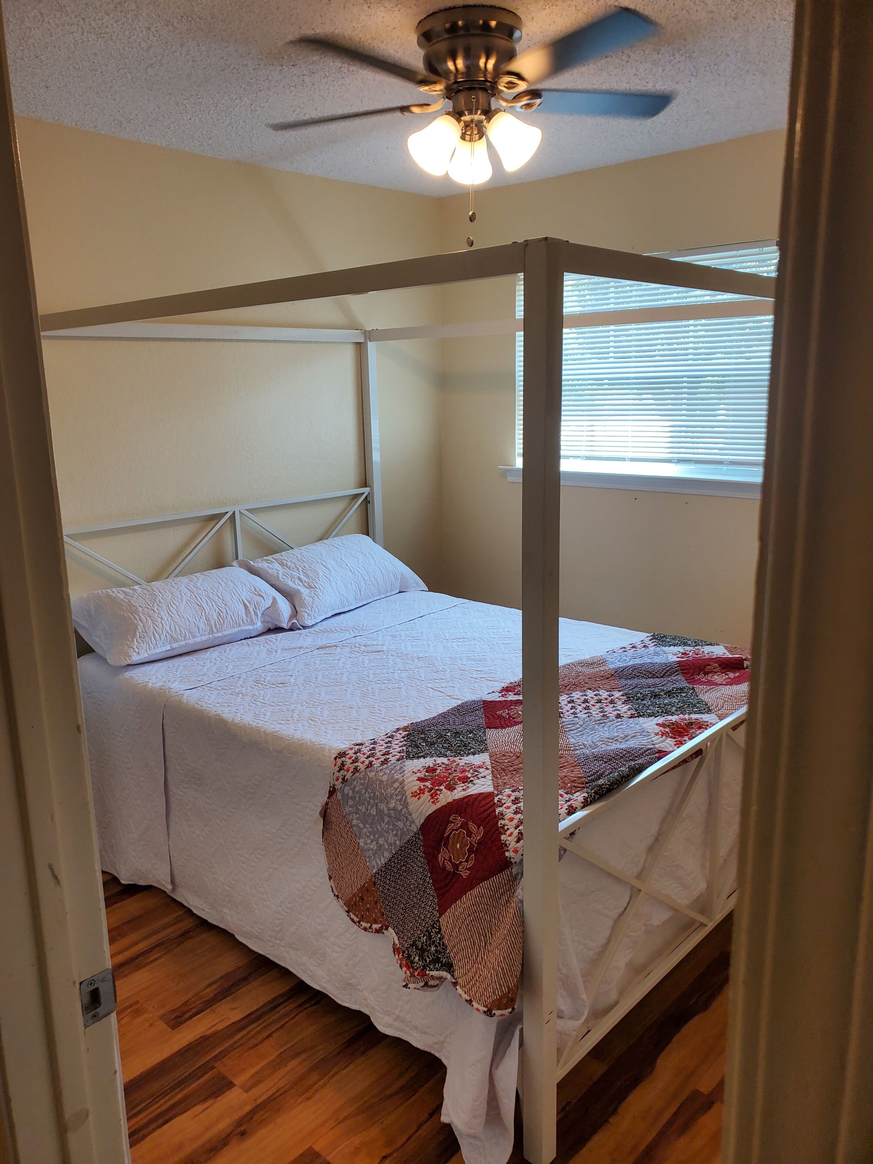 A room with a four-poster bed, a ceiling fan, and a window with blinds.