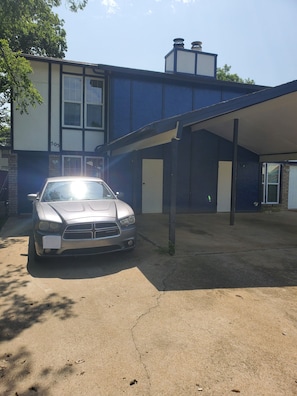 Un coche plateado estacionado en una entrada con un edificio azul al fondo.