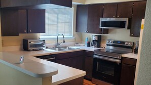 A modern kitchen with dark wooden cabinets, stainless steel appliances, and a wooden floor.