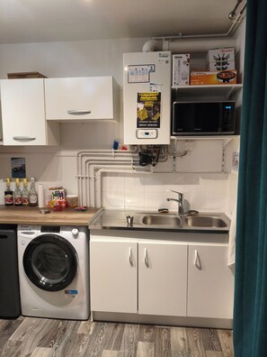 A compact kitchen with a washing machine, a microwave, and a sink. - Wellness and Relaxation Studio (La Tour-du-Pin)