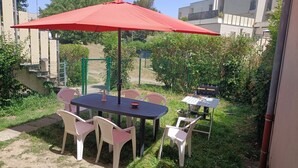 Eine Terrasse im Freien mit Tisch, Stühlen, einem roten Sonnenschirm und einem Grill.