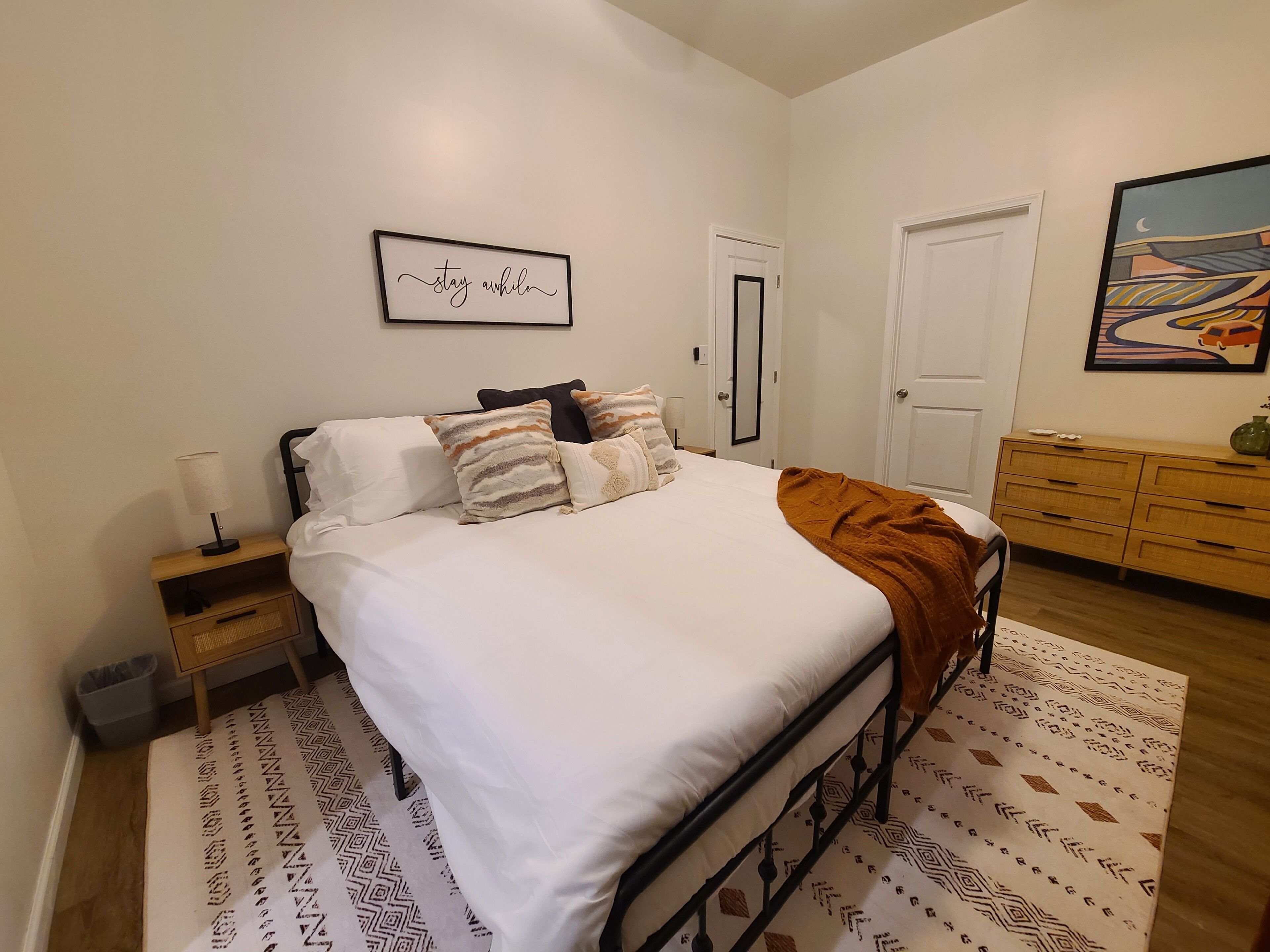 A bedroom with a bed, bedside tables, a dresser, a framed quote on the wall, and a patterned rug.