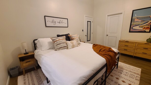 A bedroom with a bed, bedside tables, a dresser, a framed quote on the wall, and a patterned rug. - Fair Oaks Guesthouse (Conyers)