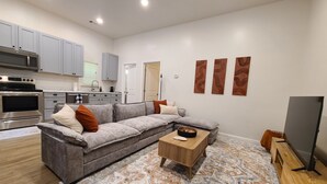 A modern living space with a grey sofa, wooden coffee table, and a flat-screen TV. - Fair Oaks Guesthouse (Conyers)