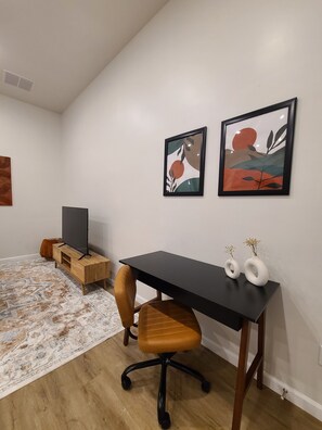 A modern living space with a black desk, a brown leather chair, a TV on a wooden stand, and two abstract paintings on the wall.