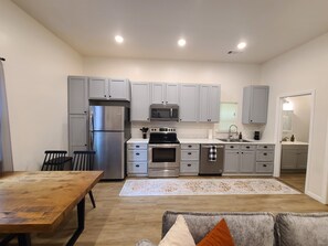 A modern kitchen with grey cabinets, stainless steel appliances, and a wooden dining table.