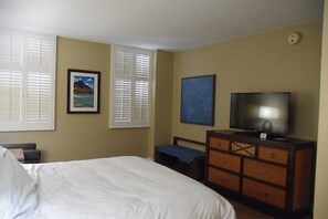 A hotel room with a bed, a television, a dresser, and two windows with shutters. - Oceanfront View in Honolulu at The Hilton Hawaiian Village Lagoon Tower (Honolulu)