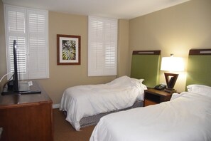 Ein Hotelzimmer mit zwei Betten, einem Schreibtisch, einer Lampe und einem gerahmten Bild an der Wand.