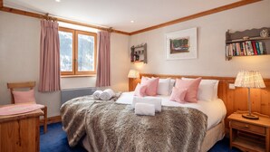 Una camera da letto con un letto grande, due comodini, una testiera in legno, una finestra con tende, una libreria e un quadro appeso al muro.