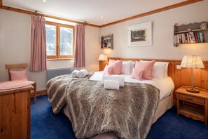 Ein Schlafzimmer mit einem großen Bett, zwei Nachttischen, einem Holz-Kopfteil, einem Fenster mit Vorhängen, einem Bücherregal und einem Gemälde an der Wand.