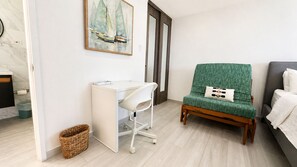 Una habitación con escritorio, una silla verde, una cama y un cuadro de veleros.