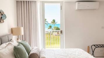 Quarto de hotel com cama, janela com cortinas e vista para o oceano, além de ar condicionado.