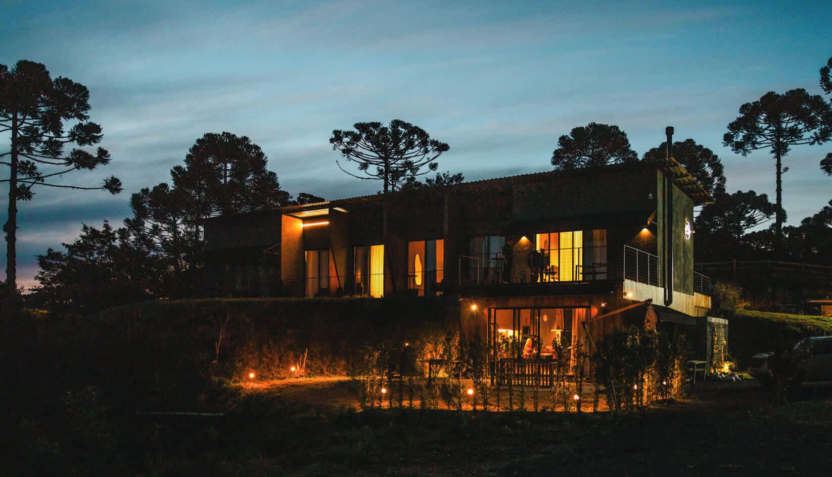 A modern two-story house with a balcony and a lit pool area at dusk.