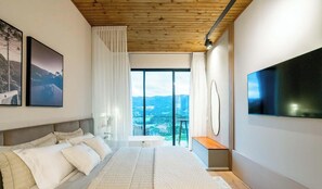 Ein modernes Schlafzimmer mit einem großen Bett, Blick ins Freie und einem Flachbildfernseher.