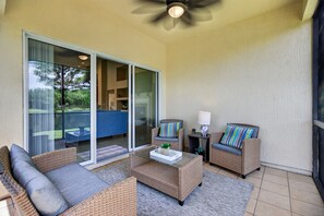 A sunlit patio with wicker furniture, a glass door leading to a deck, and a ceiling fan.