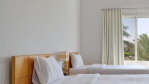 A hotel room with a wooden bed, white bedding, a window with curtains, and a view of palm trees.