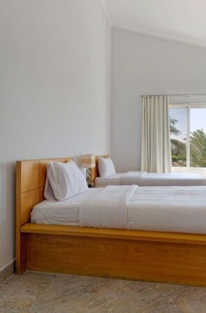 A hotel room with a wooden bed, white bedding, a window with curtains, and a view of palm trees.