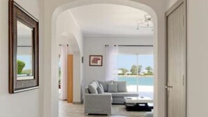A hallway leading to a living area with a grey sofa, a framed picture on the wall, and a view of the outdoors.