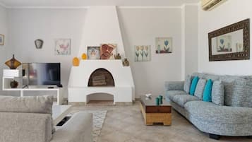 Een woonkamer met een open haard, een bank, een televisie en kunst aan de muren.