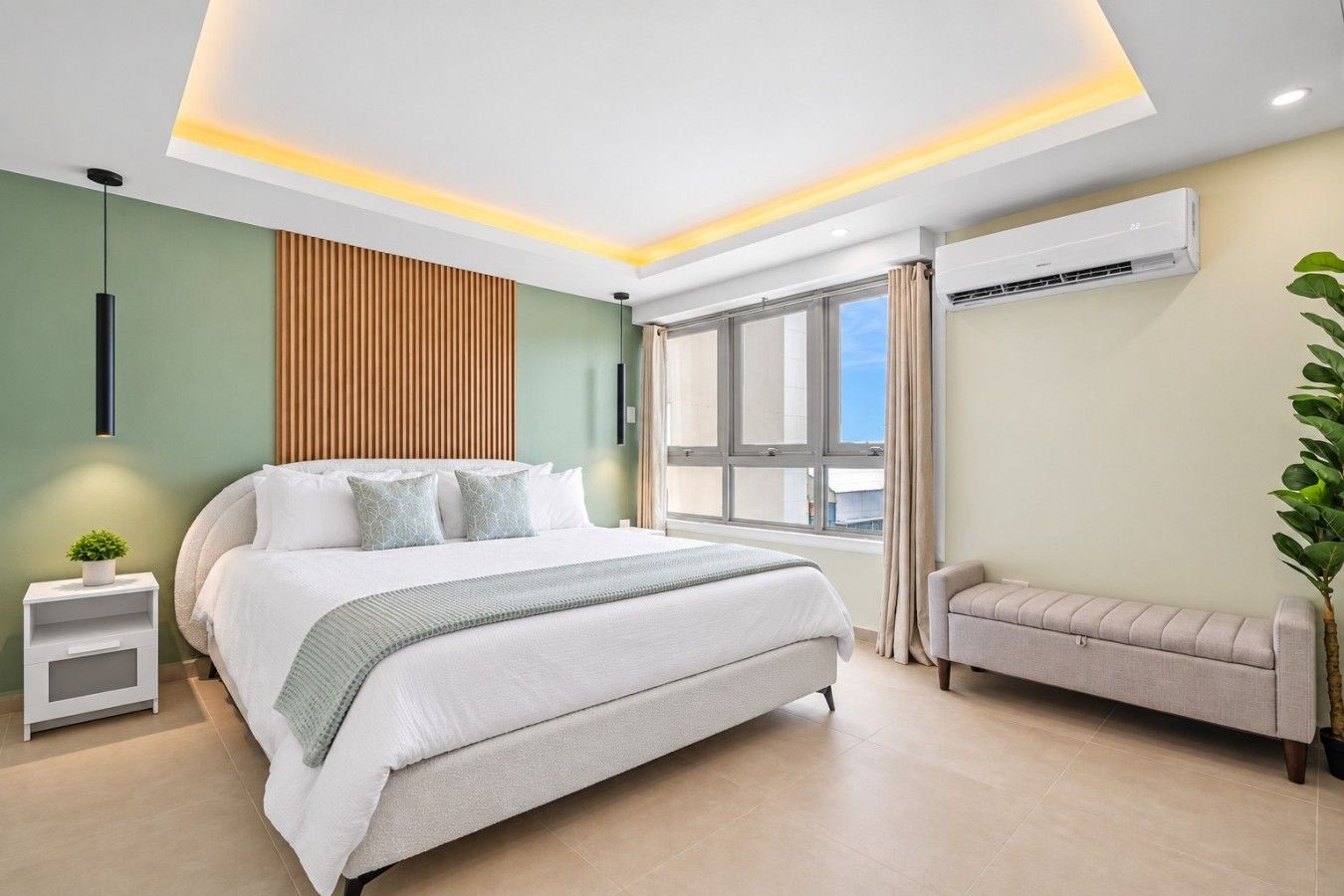 A modern bedroom with a large bed, bedside tables, a bench, and an air conditioning unit.