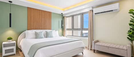 A modern bedroom with a large bed, bedside tables, a bench, and an air conditioning unit.