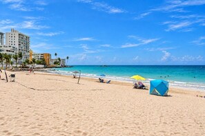 A beach with a clear sky, a sandy shore, and a building in the background. - Remodeled Isla Verde Condo • One block to Beach (Carolina)