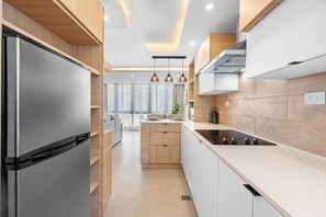 Eine moderne Küche mit Einbaukühlschrank, einer zentralen Kochinsel, Pendelleuchten und Blick zum Wohnbereich.