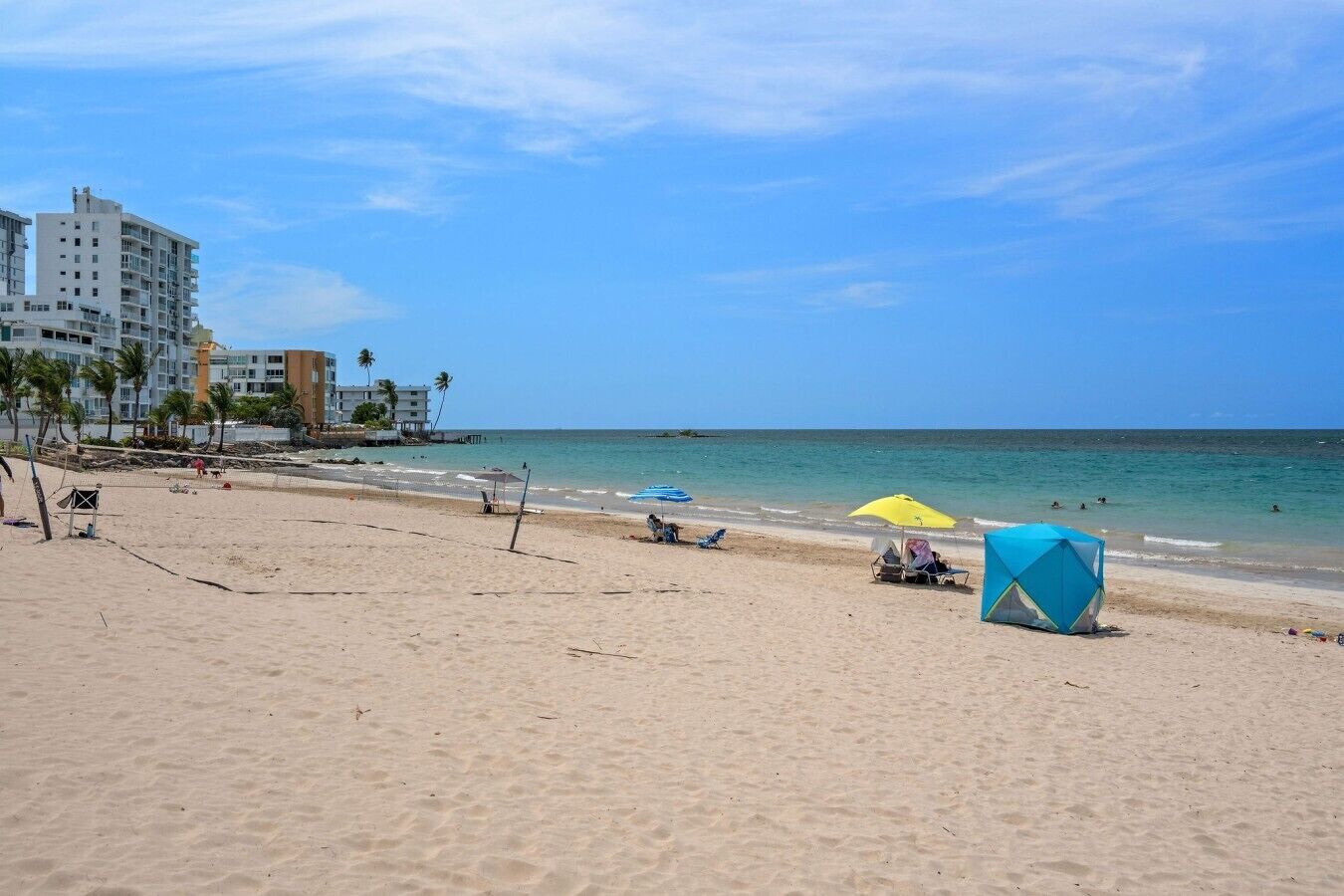 Une plage avec un filet de volley-ball, des parasols et une tente.