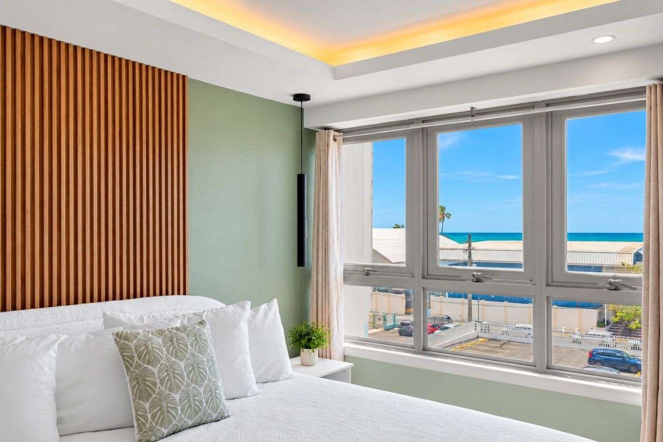 A hotel room with a bed, a view of the beach, and a window with a view of the street.