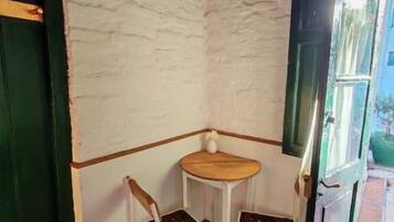 Una habitación de esquina con una pared blanca texturizada, una pequeña mesa de madera, dos sillas blancas y una puerta verde.