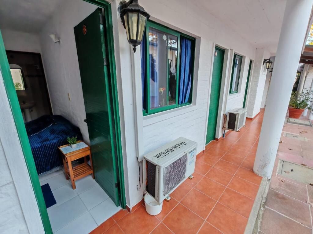 Un pasillo con varias habitaciones, cada una con ventana y puerta. Cerca de la entrada de una habitación hay una pequeña mesa con una planta.