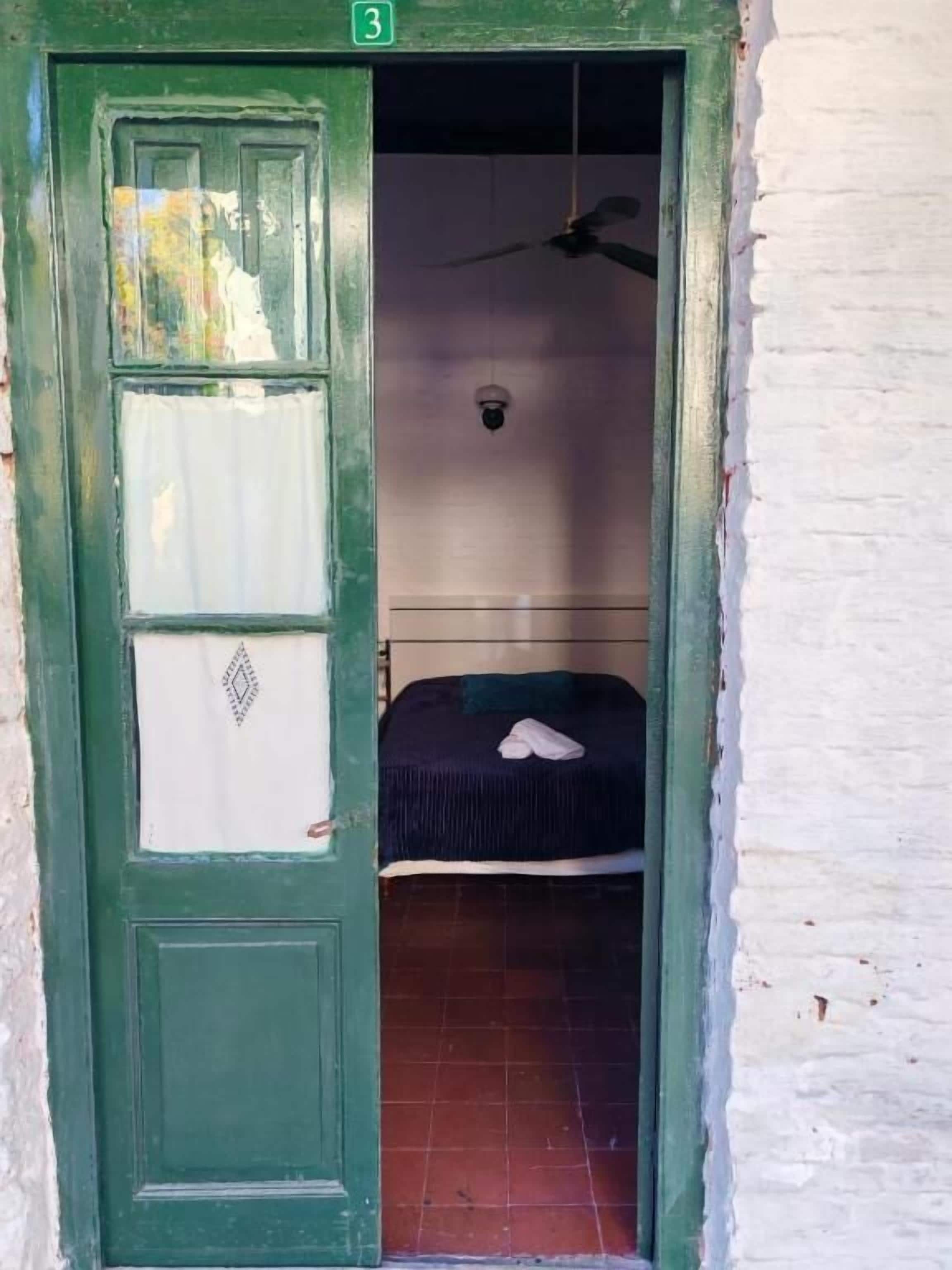 Una habitación con puerta verde, una cama y un ventilador de techo.
