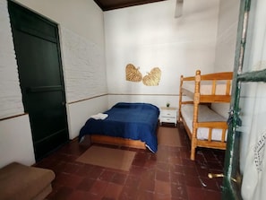 Een slaapkamer met een bed, een houten stapelbed, een nachtkastje, een groene deur en een bruine bank.