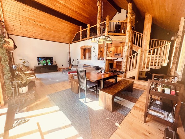 Un amplio salón con una escalera de madera, una mesa de comedor y un televisor.