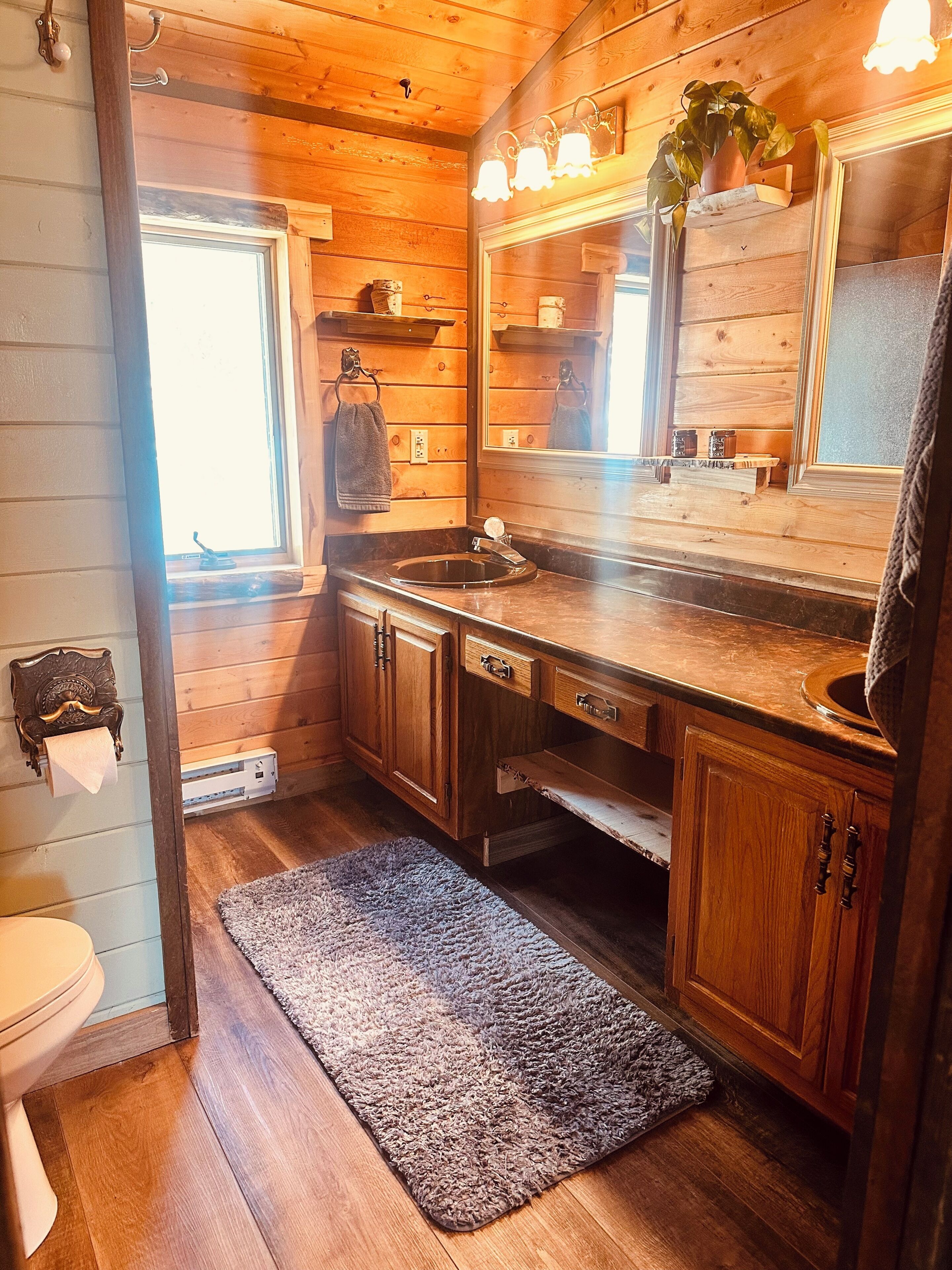 Baño de cabaña de madera con lavamanos, espejo, toallero y una ventana pequeña.