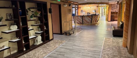 Een hotelgang met houten kasten waarin diverse objecten staan, een receptiebalie en een zithoek.