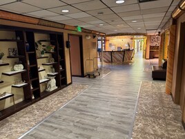 Un pasillo de hotel con estanterías de madera que exhiben distintos objetos, un mostrador de recepción y una zona de estar.