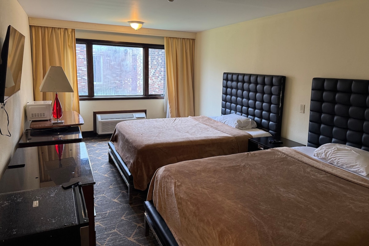 A hotel room with two beds, a desk, a lamp, and a window with curtains.