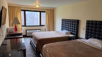 Habitación de hotel con dos camas, un escritorio, una lámpara y un ventanal con cortinas.