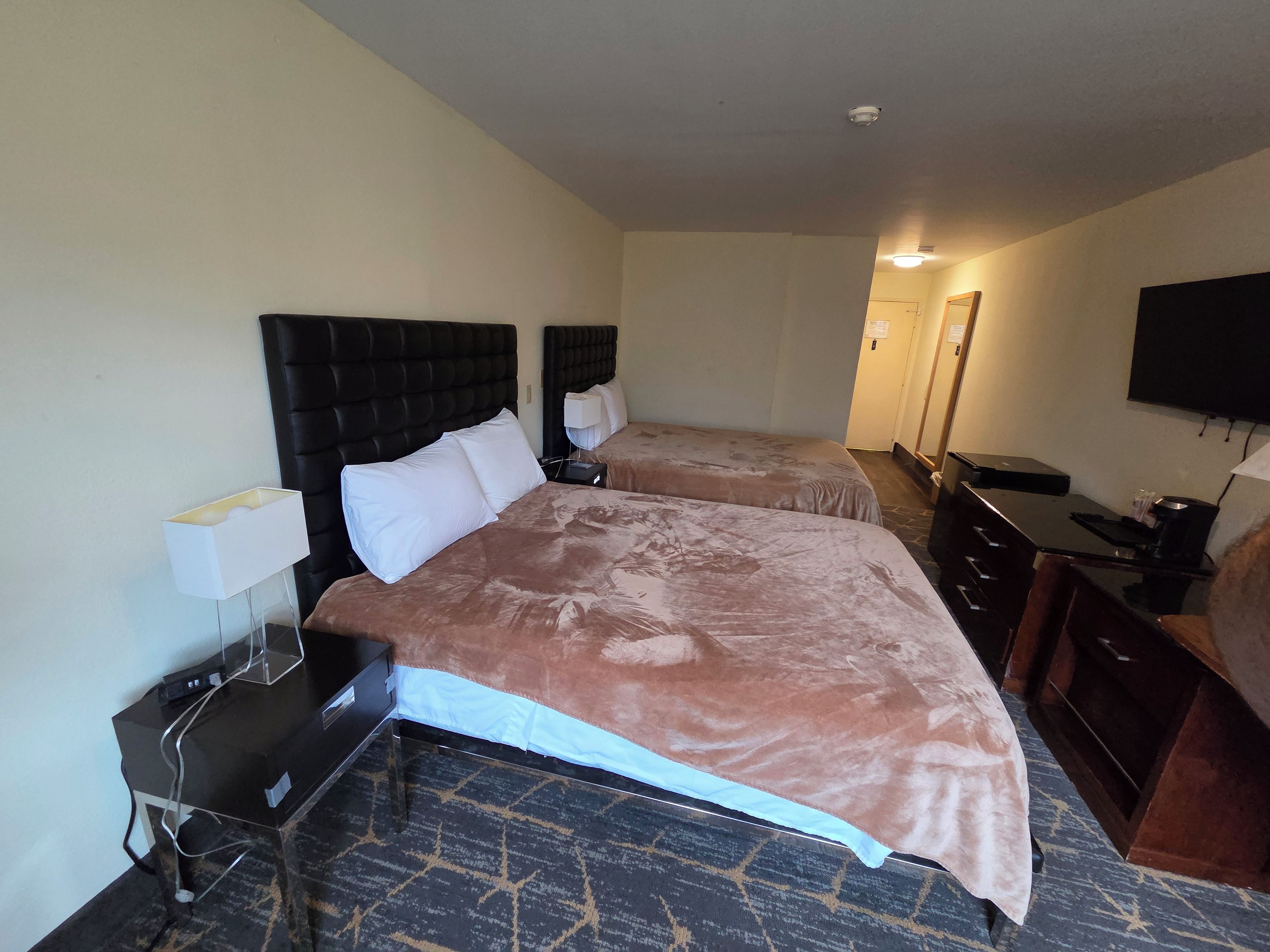 A hotel room with two beds, a desk, a flat-screen TV, and a mirror.
