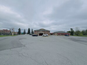 A parking lot with several cars, a building with a sign for Hilltop Inn, and a fenced area with trees. - HILLTOP INN (Barre)