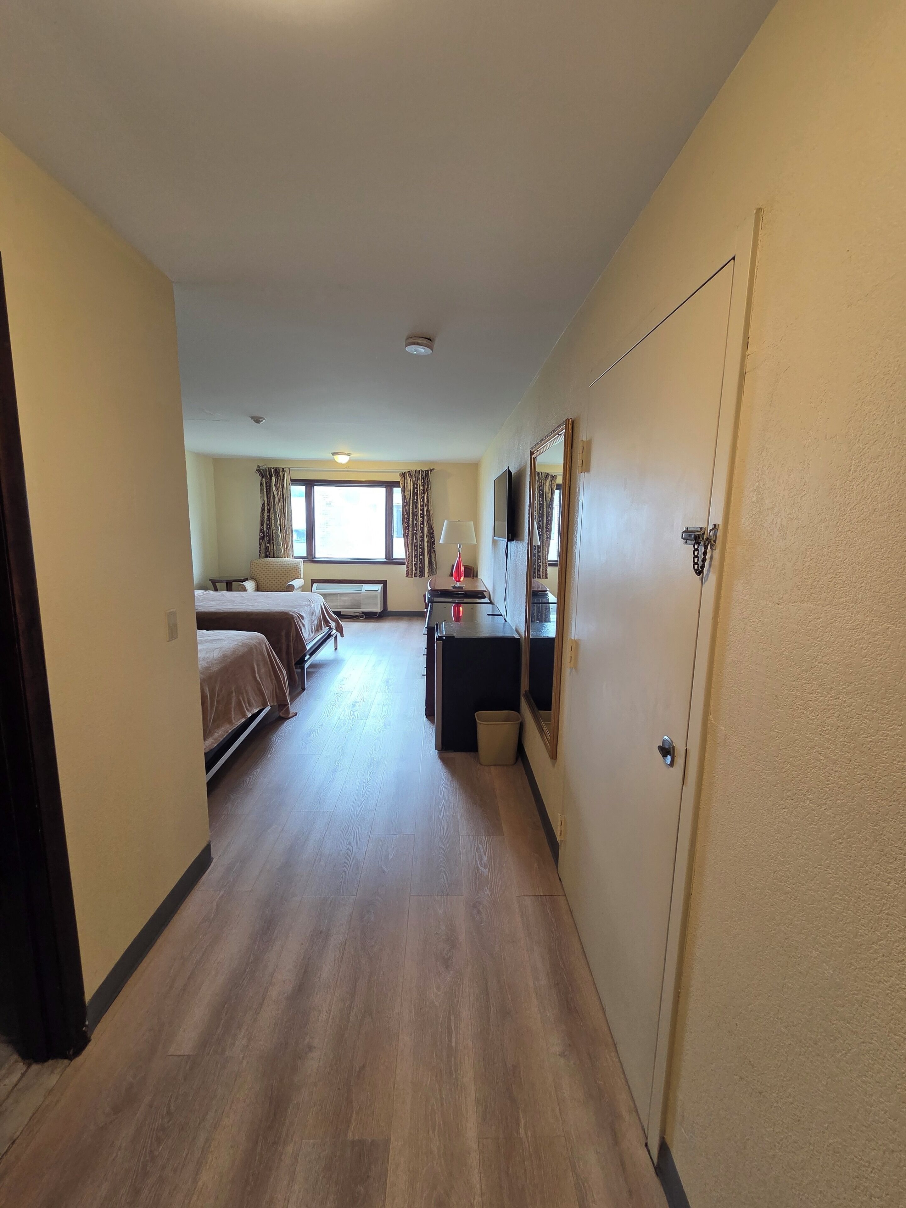 Habitación de hotel con cama, escritorio, silla, televisor y ventana con cortinas.