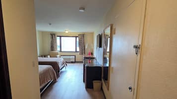 A hotel room with a bed, a desk, a chair, a TV, and a window with curtains.