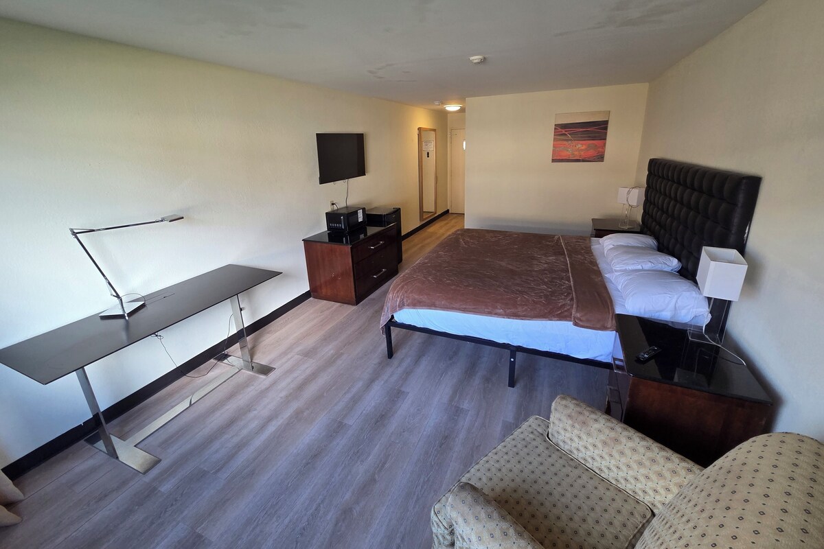 A hotel room with a bed, a desk, a chair, a dresser, and a television.