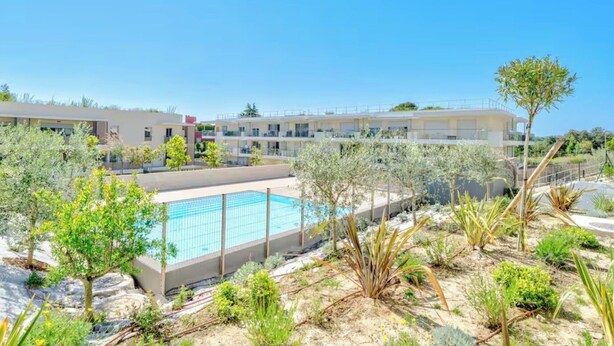 Um hotel com piscina, rodeado por jardins bem cuidados e um céu azul límpido.