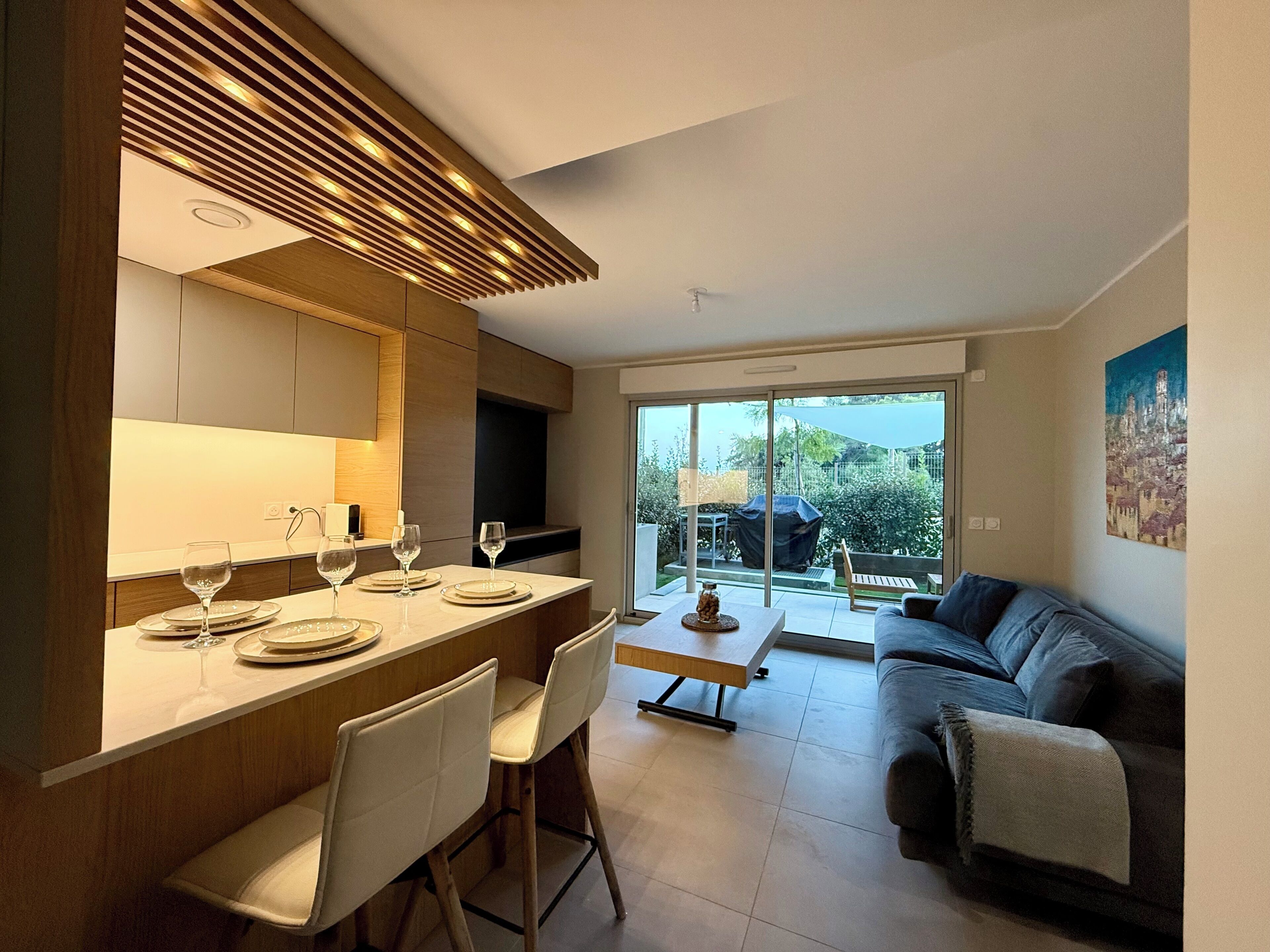 A modern kitchen with a dining area, a sofa, and a view of the outdoors.