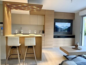 Eine moderne Küche mit integriertem Fernseher, Holz-Barhocker und einer Sitzecke mit Bergblick.