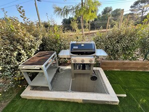 Ein tragbarer Grill mit Metallrost und Bedienelementen, auf einer Betonplatte mit einer Metall-Abdeckung platziert.
