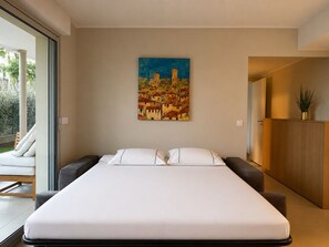 Een moderne slaapkamer met een groot bed, een schilderij van een stadsgezicht en uitzicht op groen door een schuifdeur.