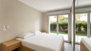 Quarto moderno com uma cama grande, mesa de cabeceira de madeira e porta de vidro deslizante para um jardim.